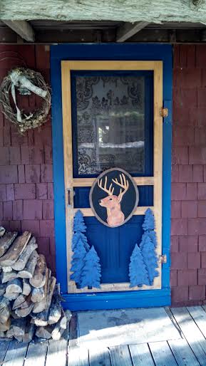 carved and painted wood screen door with deer medallion and pine trees